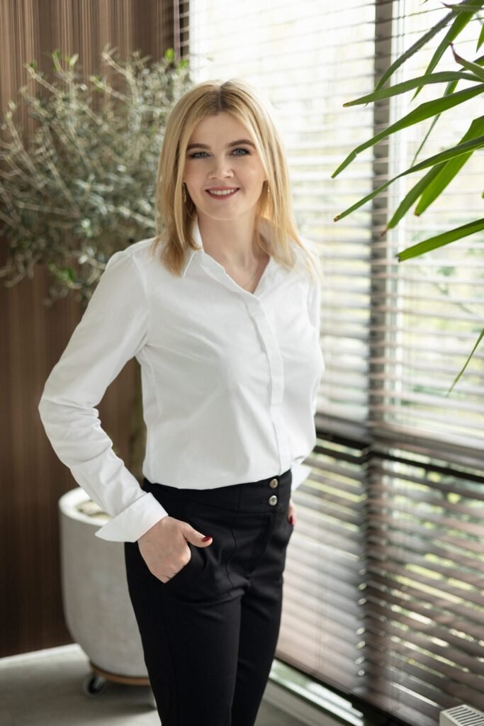 Małgorzata Jaszczyk w białej koszuli przy oknie